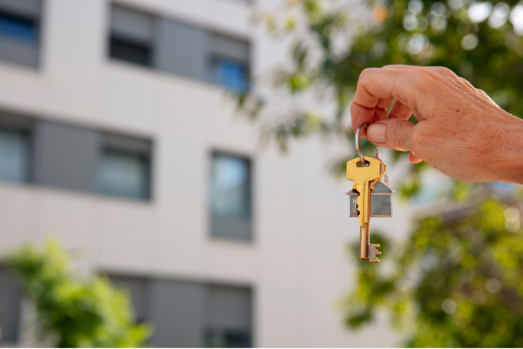 Photo prise devant un batiment, au premier plan, une main tenant des clés