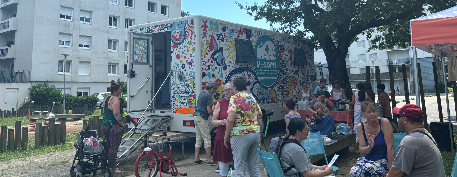 Photo prise devant une résidence Silène lors d'un événement Silène. Au premier plan, on voit l'unité mobile le MarSOINS, avec des bénévoles et des locataires.