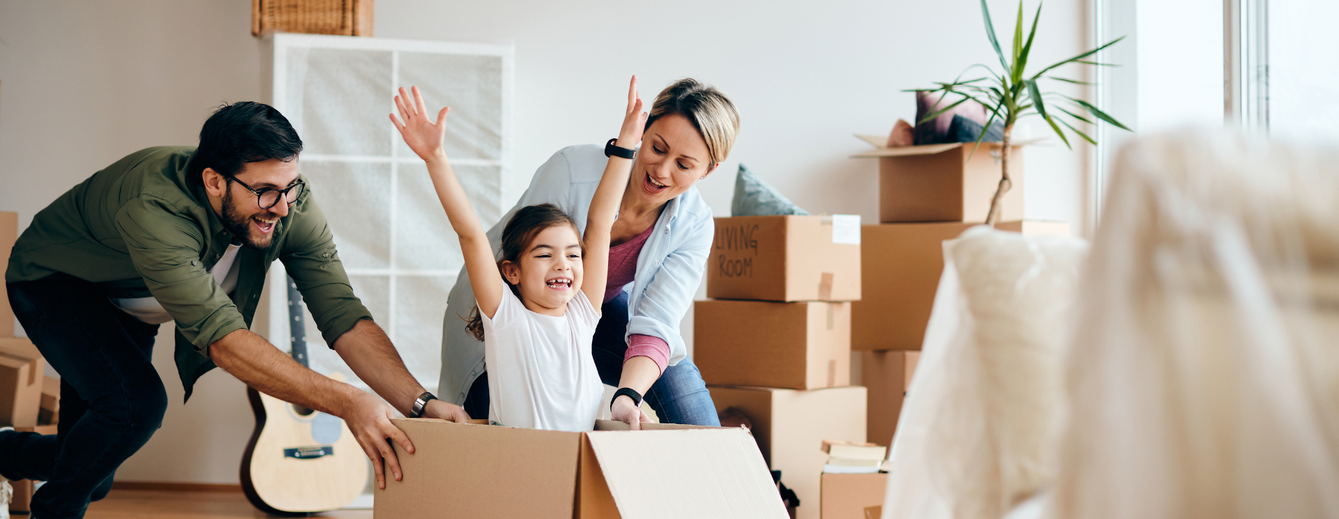 photo représentant une famille dans son salon qui emménage dans leur nouvelle maison : parents et une petite fille dans un carton.