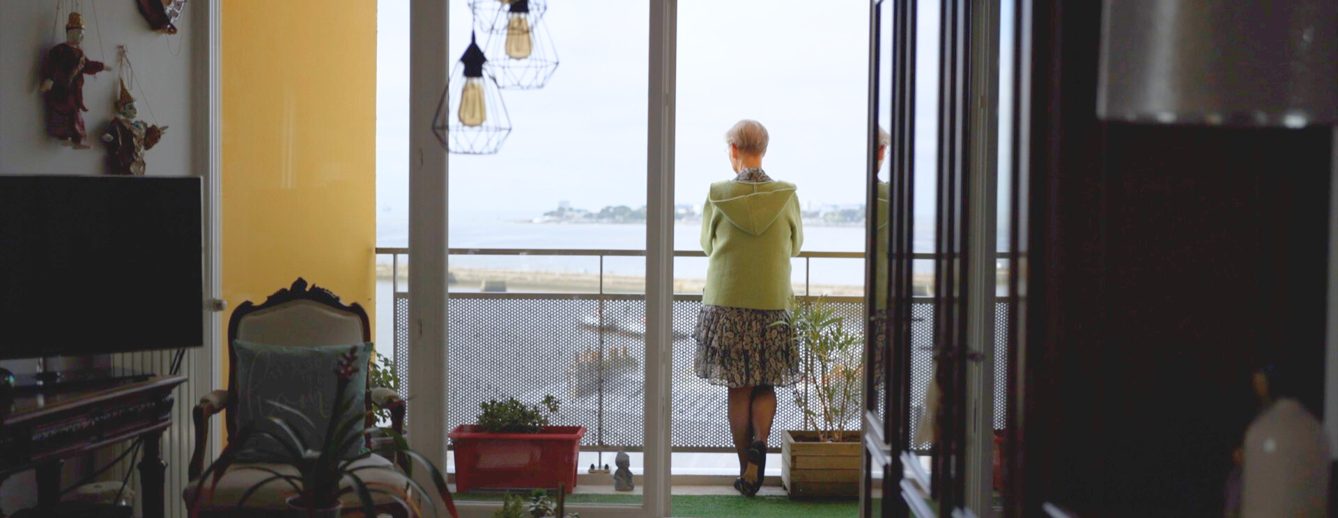 Photo de l'intérieur d'un logement silène donnant sur le balcon ouvert, avec une femme admirant la mer, à Saint-Nazaire