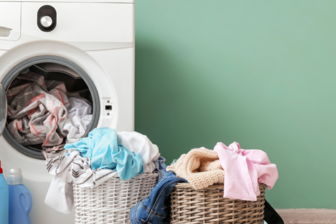 Photo d'une machine à laver devant un mur vert, avec deux petits paniers à linge rempli juste devant.