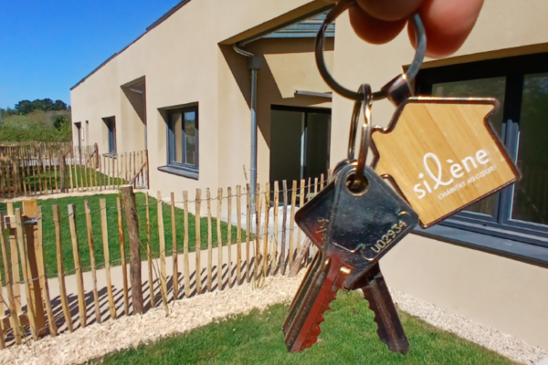 Photo prise devant une résidence neuve Silène et le jardin. Au premier plan, une main tient des clés.