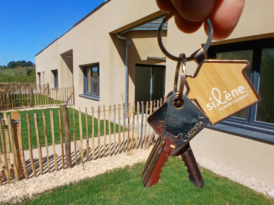 Photo prise devant une résidence neuve Silène et le jardin. Au premier plan, une main tient des clés.